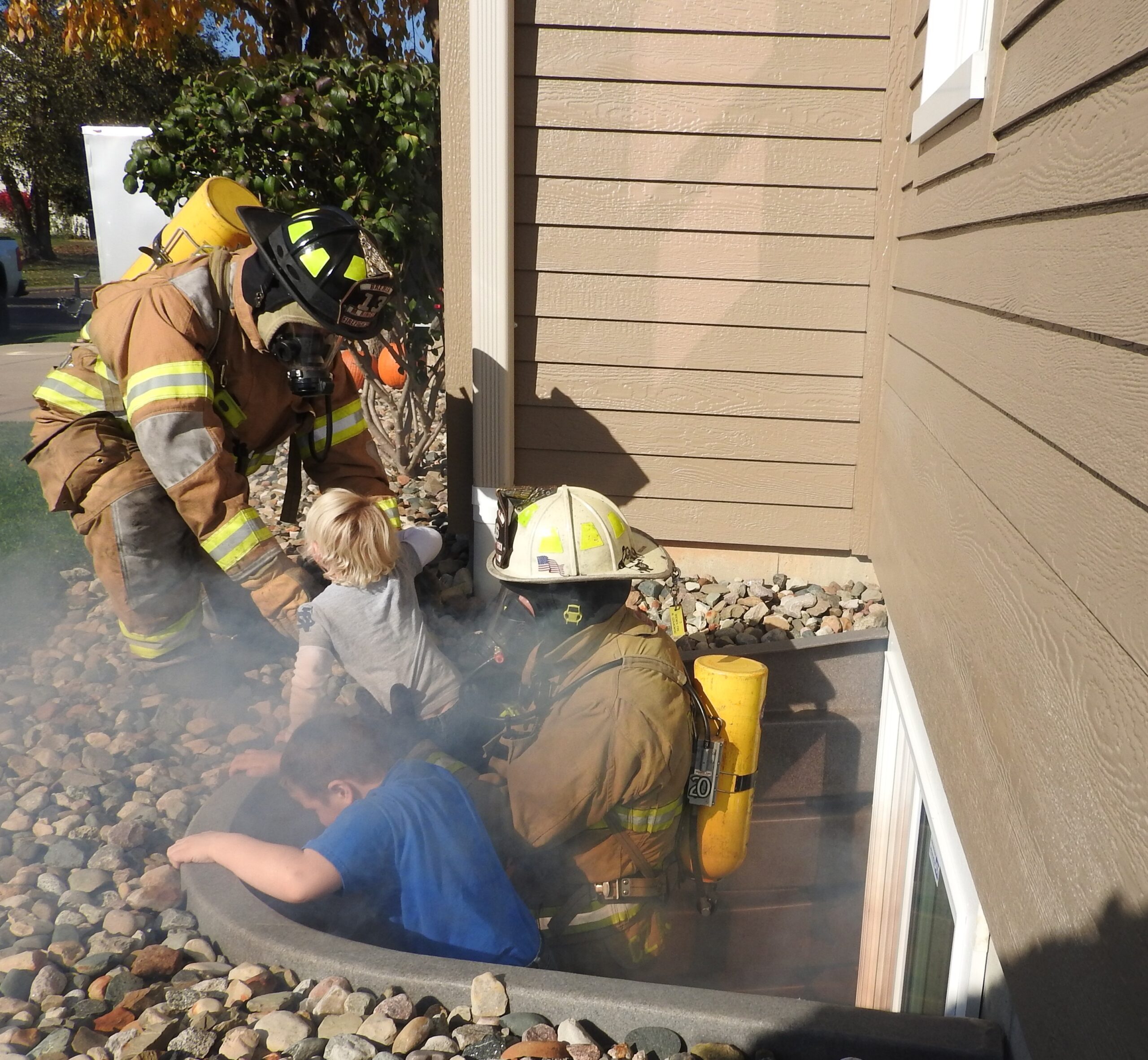 Firefighters at a basement egress window well demonstrating emergency rescue access.